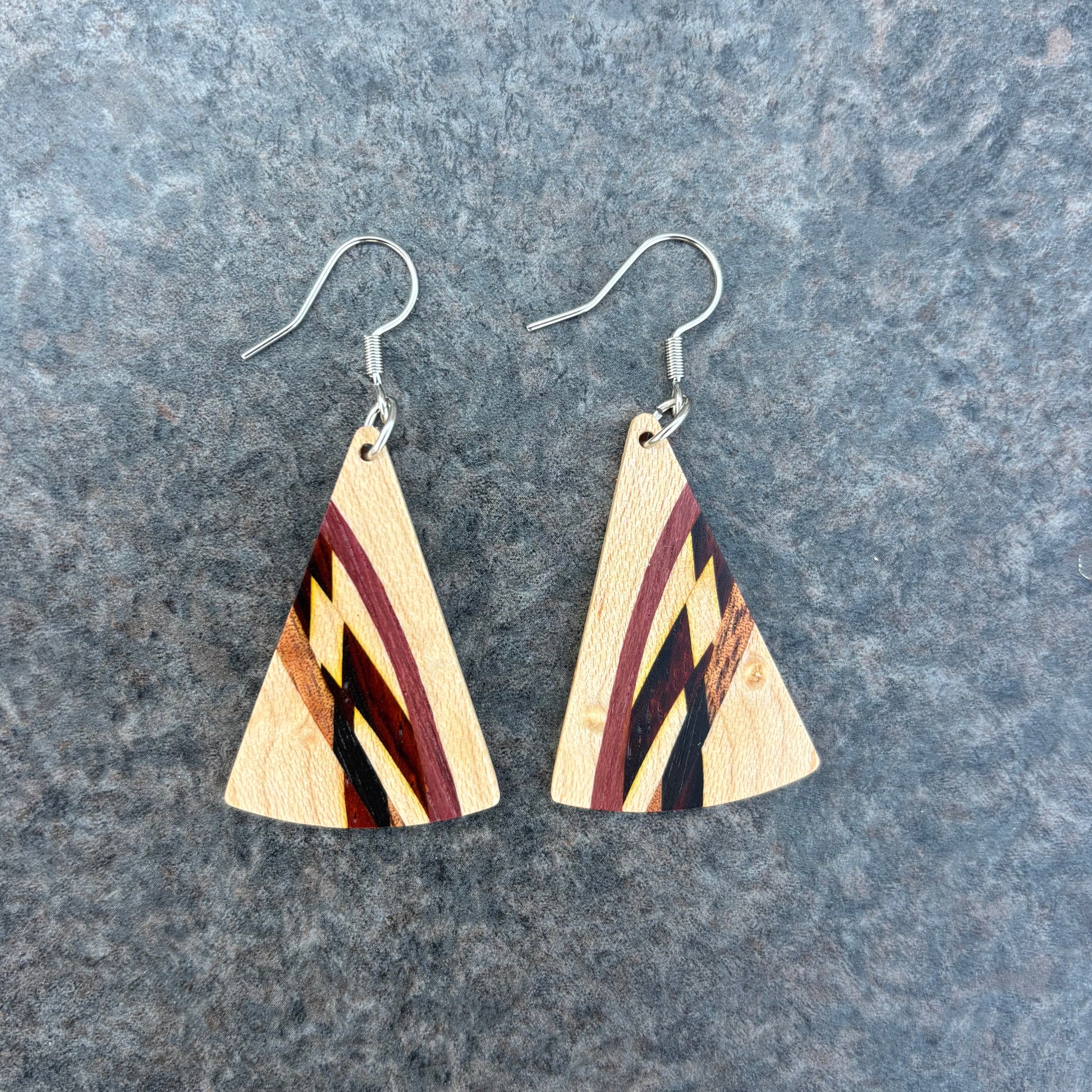 Wooden triangle earrings with a striped pattern on a gray surface