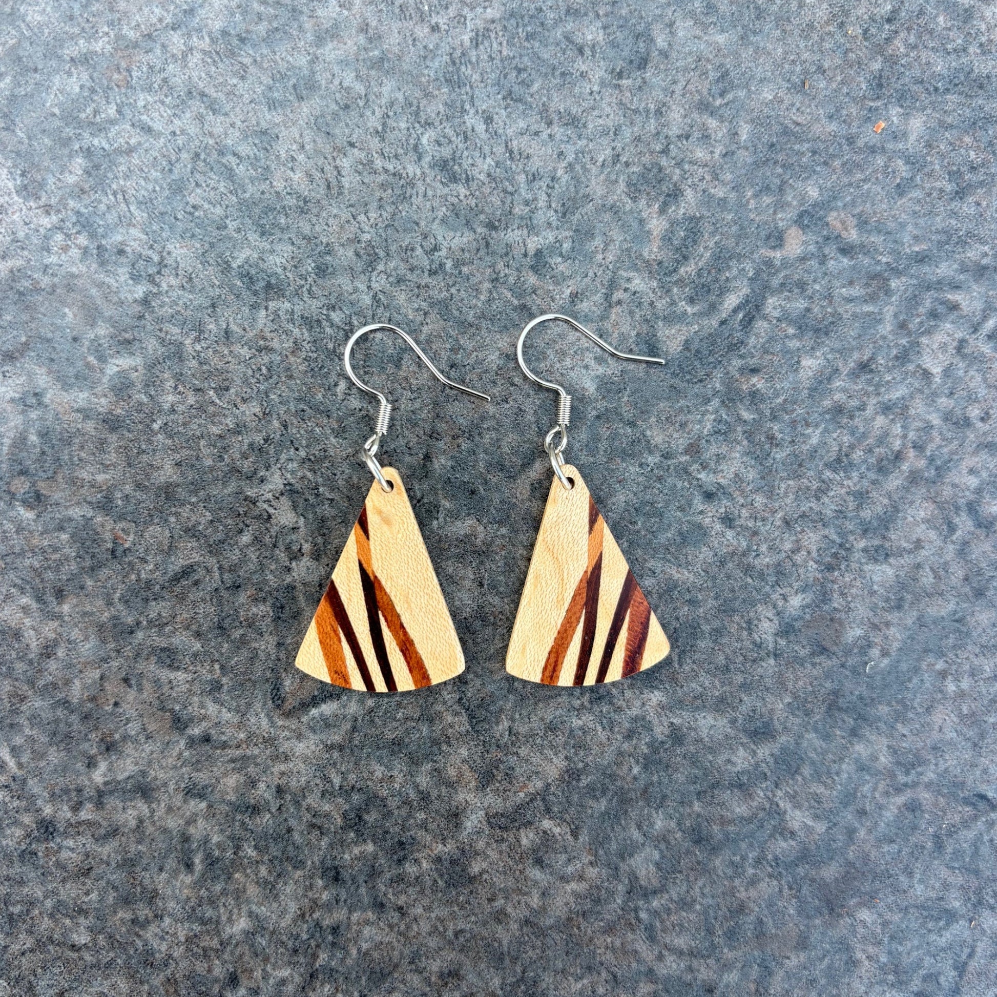 Wooden triangle earrings with striped design on a gray surface
